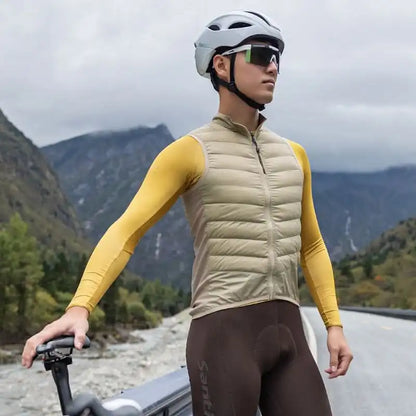 Mann i beige vattert sykkelvest, gul langermet sykkeltrøye og hvit hjelm i et fjellandskap.