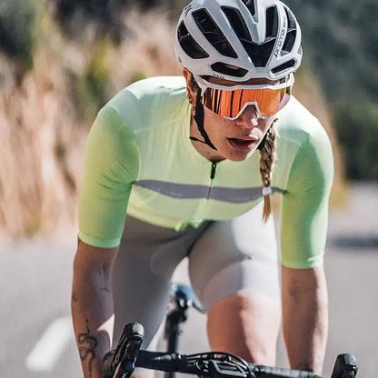 Kvinne på landeveissykkel iført hvit Kask Protone hjelm, oransje sportsbriller og limegrønn sykkeltrøye.