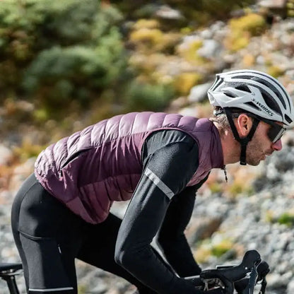 Mann på sykkel iført en lilla isolert sykkelvest og hvit S-Works hjelm i et fjellandskap.