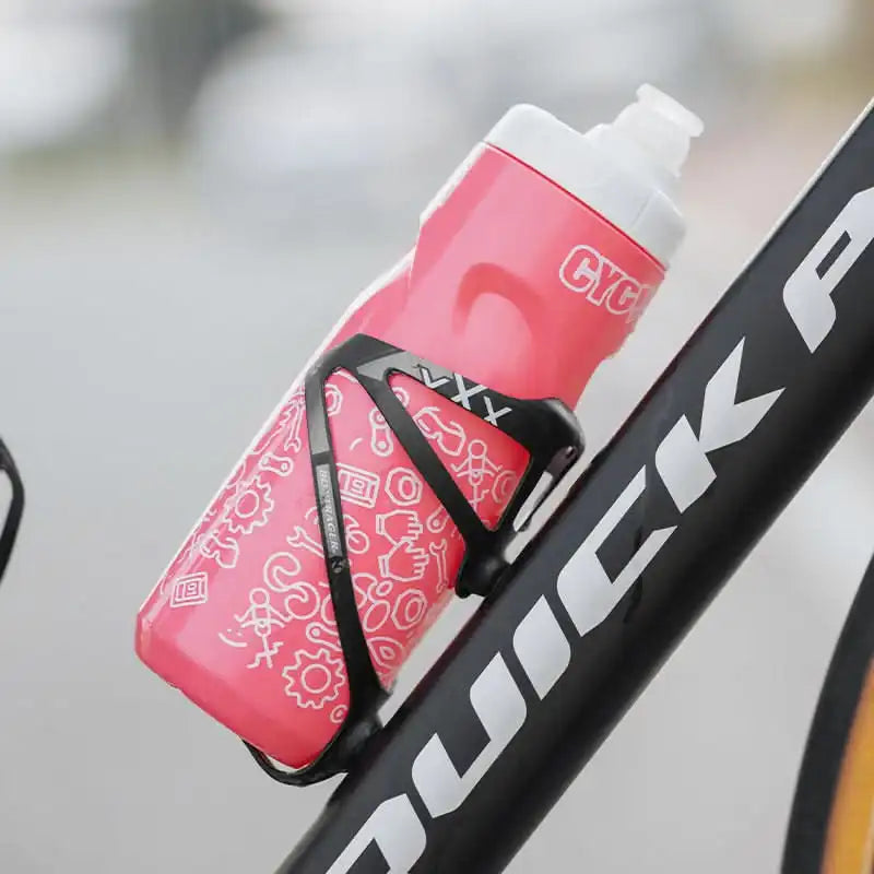 Rosa sykkelflaske med hvite illustrasjoner i en svart Bontrager flaskeholder montert på en sykkelramme.