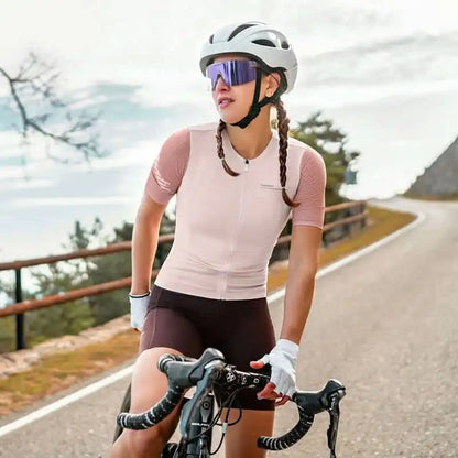Kvinne i rosa Santic sykkeltrøye og mørke sykkelshorts på landeveissykkel med hvit hjelm og lilla sportsbriller.