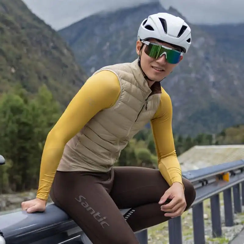 Syklist i beige Santic sykkelvest, gul langermet trøye og brun sykkelbukse i fjellandskap.