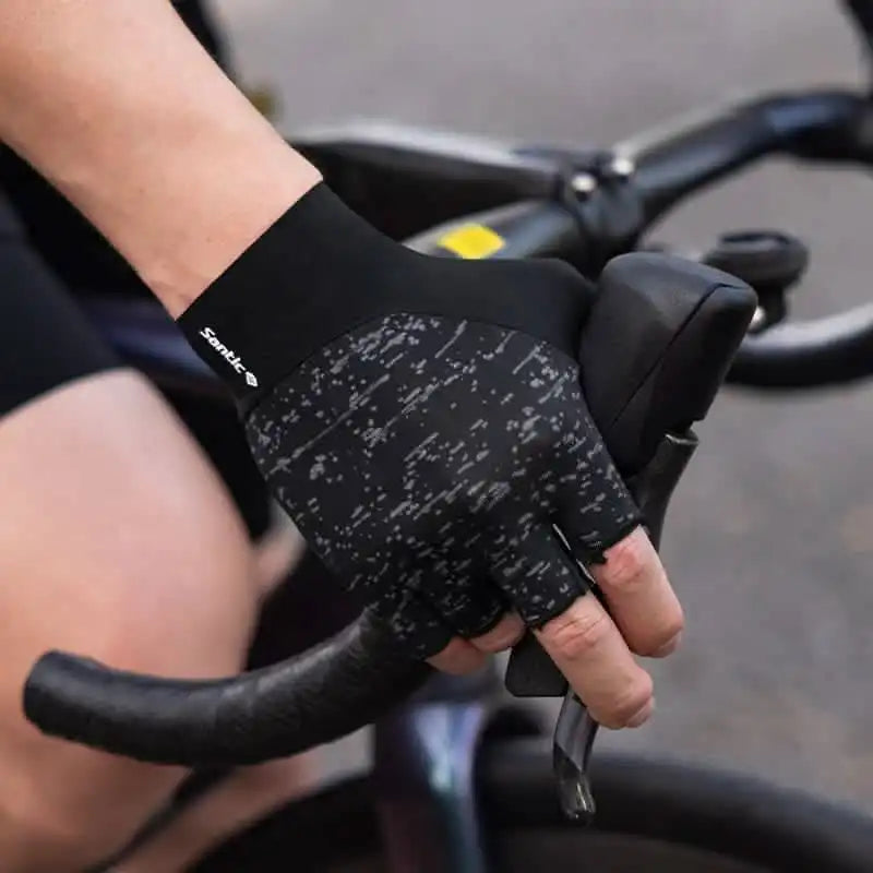 Santic halvfinger sykkelhansker i svart med mønster, vist mens de holder i et sykkelstyre.