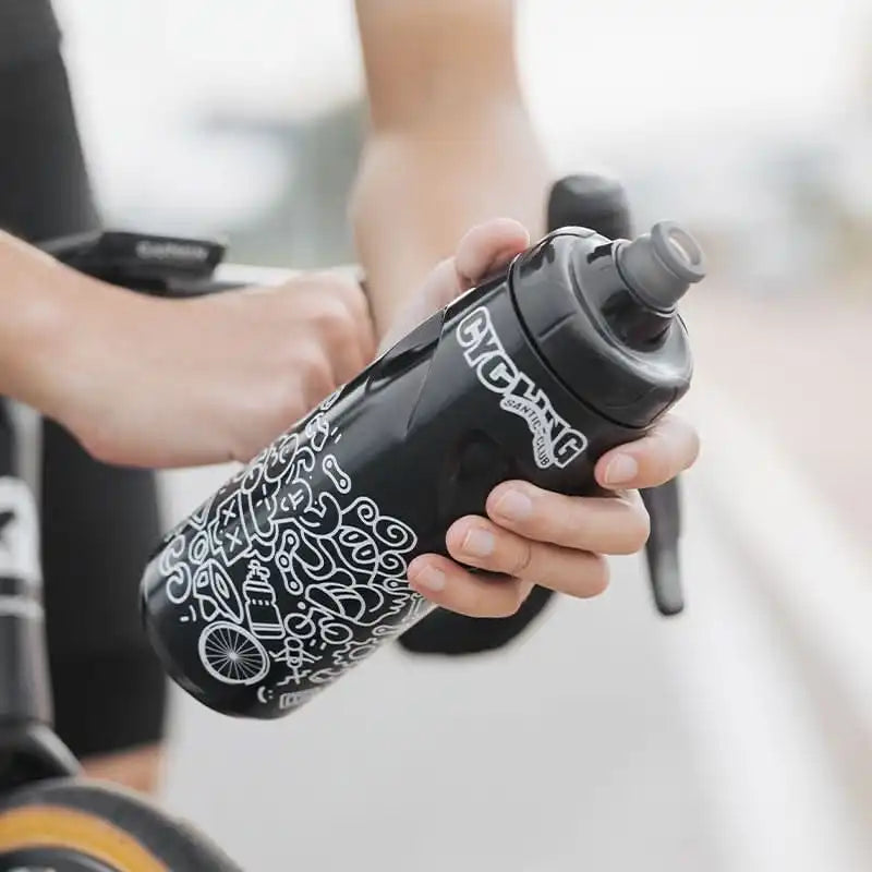 En person som holder en sort drikkeflaske til sykkel med hvite illustrasjoner og teksten Cycling.