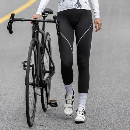 Kvinne i svart sykkeltights med hvite detaljer står ved siden av en landeveissykkel på asfalt.