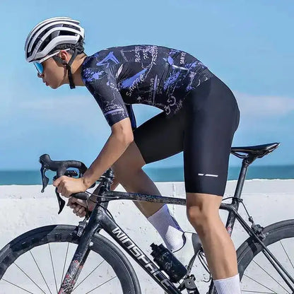 En mannlig syklist i mønstret sykkeltrøye og sorte bib-shorts på en Winspace landeveissykkel ved kysten.